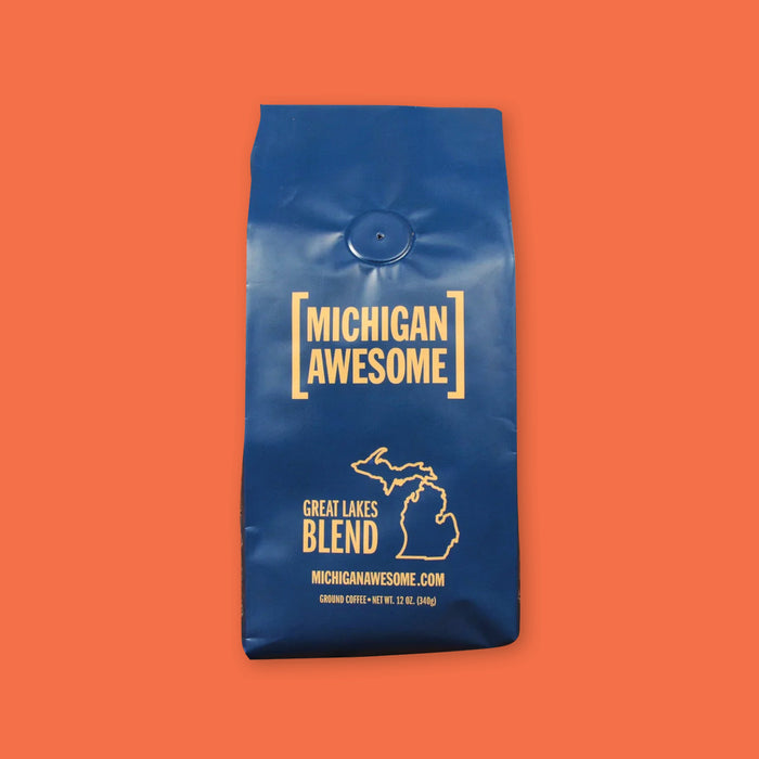 On a coral orange background sits a navy bag of Michigan Awesome Coffee is a Great Lakes Blend. 12 oz (350g). 