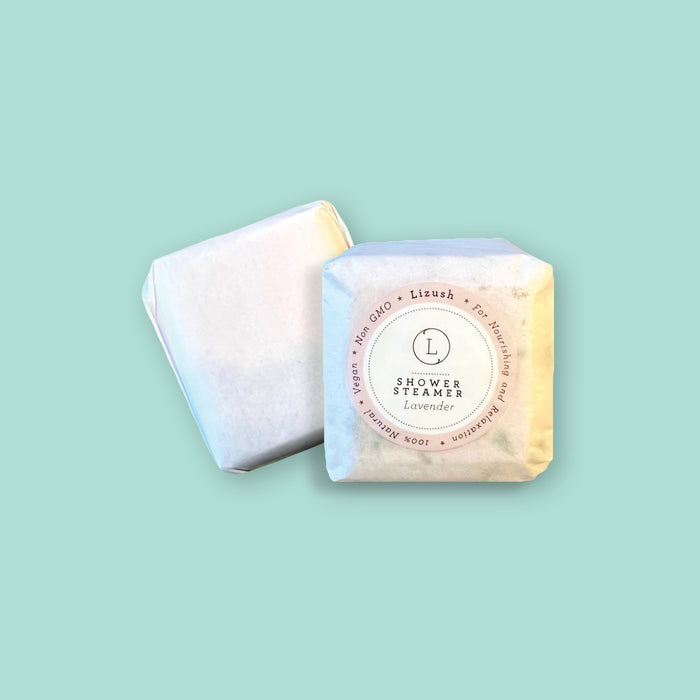 On a seafoam background sits a packaged Lavender Shower Steamer from Lizush. It is "For Nourishing and Relaxation, 100% Natural, Vegan, and Non GMO."