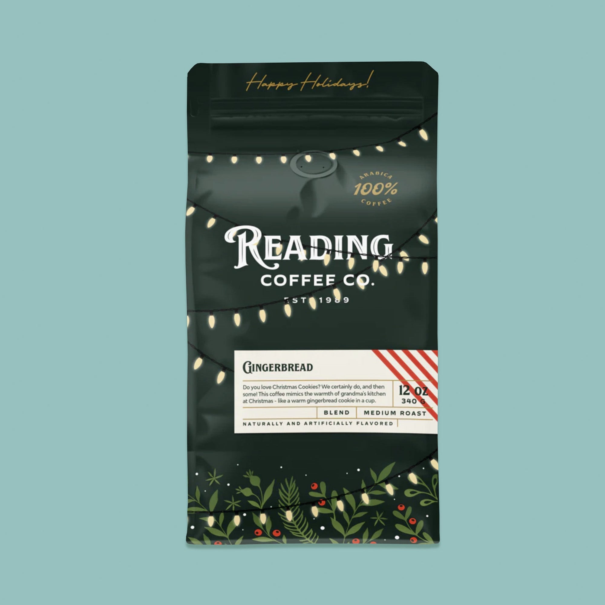 On a sage green background sits a dark green package of coffee. This package is gold, white, and dark green lettering. There are swags of lights and greenery with berries. It says "Happy Holidays!", "Reading Coffee Co. Est. 1989", "Gingerbread Blend Medium Roast." It is '100% Arabica Coffee. It also says "Do you love Christmas Cookies? We certanily do, and then some! This coffee mimics the warmth of Grandma's kitchen at Christmas - like a warm gingerbread cookie in a cup." 12 oz 340g
