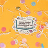 On a sunny mustard background sits a sticker with white crinkle and big, colorful confetti scattered around. This colorful sticker has an illustration of an open book and handdrawn doodles. It says "forever chasing the high of the scholastic book fair" in black, thick serif lettering.