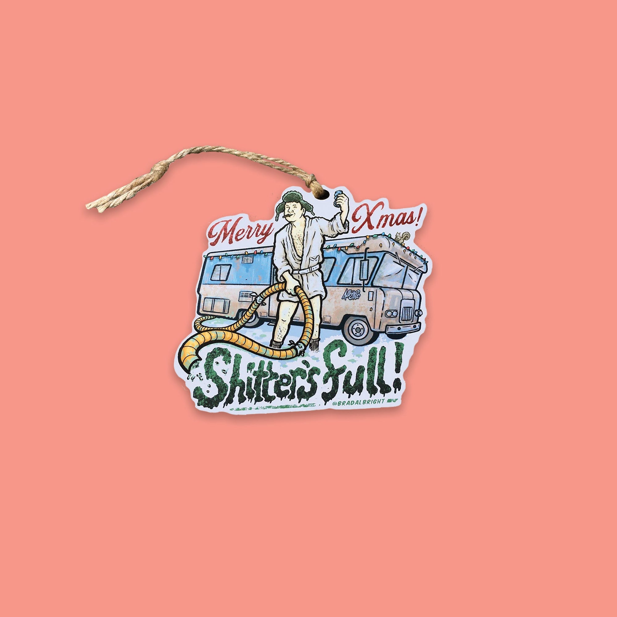 On a coral pink background sits an ornament. This Griswold Family Vacation themed wood ornament is of Cousin Eddie's motorhome. He's standing outside in his robe and hat, holding a hose and a beer and it says "Merry Xmas Shitter's Full."