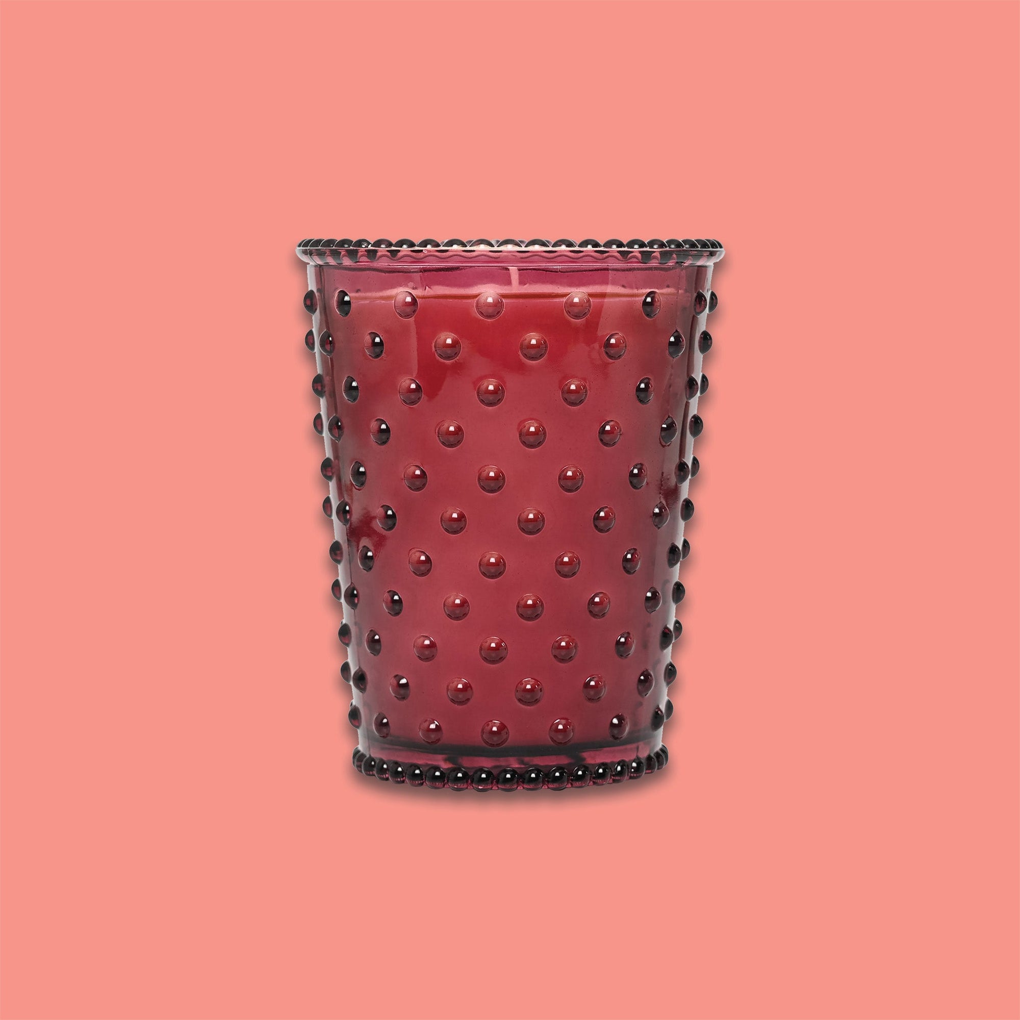 On a coral background sits a red hobglass candle. 