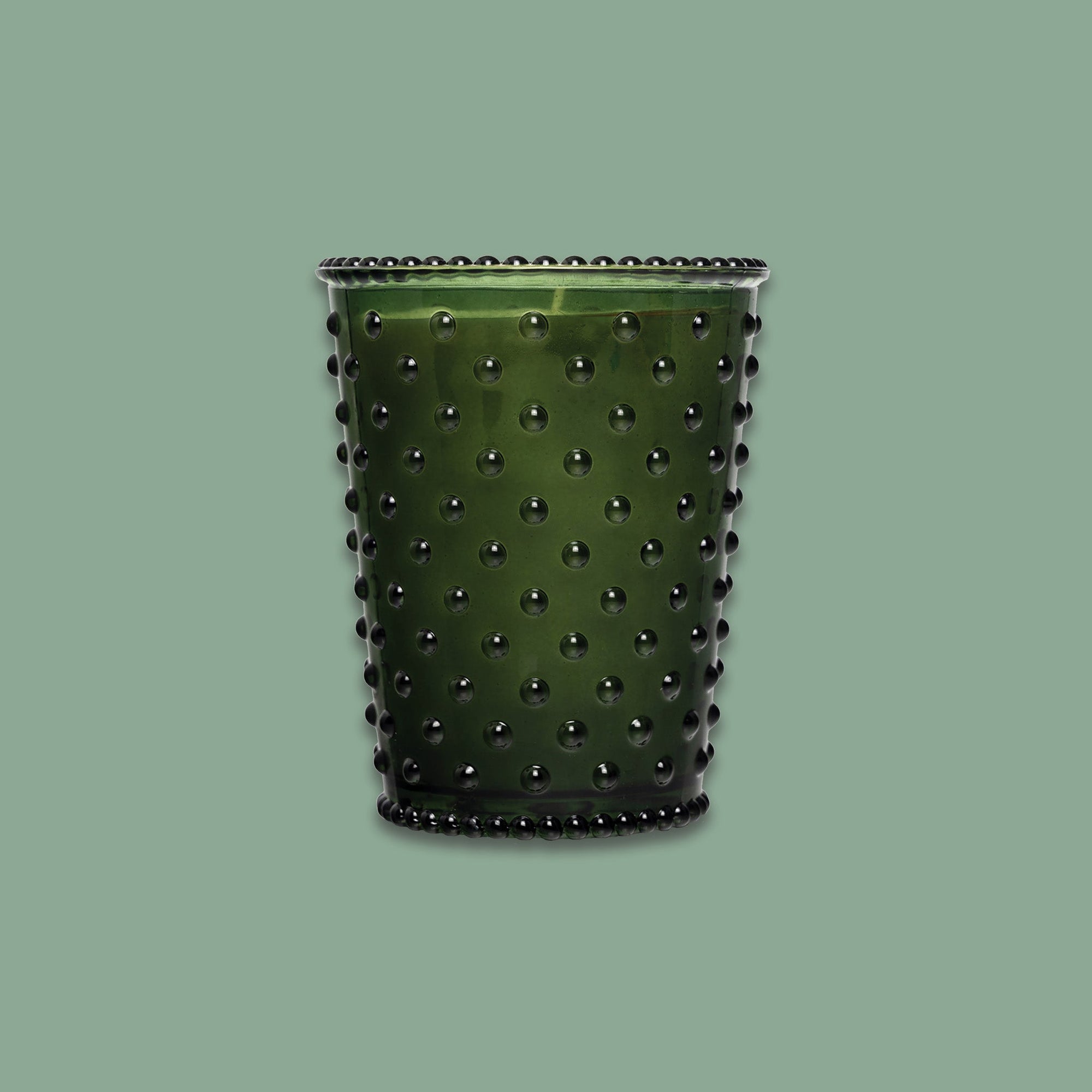 On a sage green background sits a dark green hobglass candle.