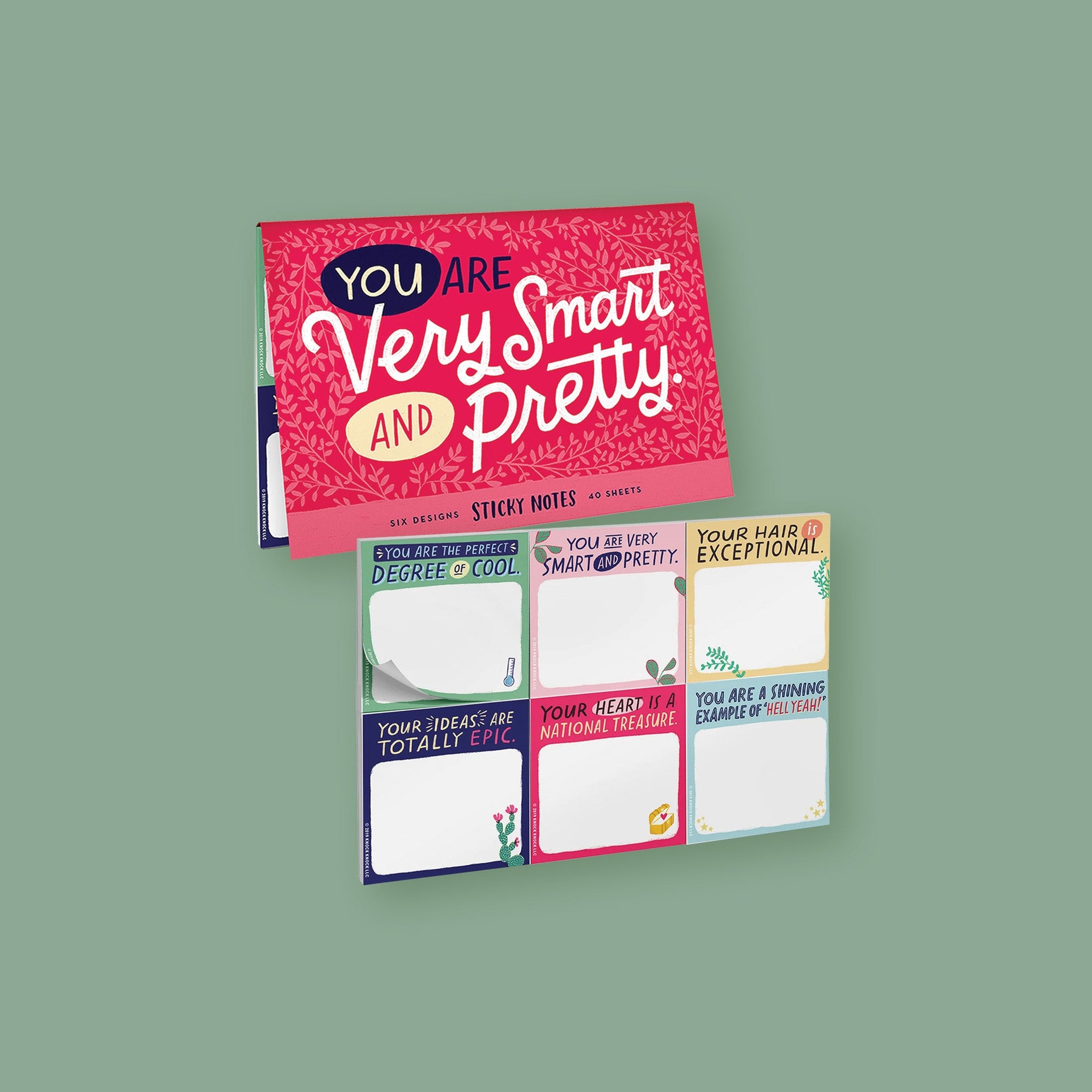 On a moss green background sits a packet. This is a close-up of a cherry pink packet of sticky notes that has light pink illustrations of branches with leaves. It says "YOU ARE Very Smart AND Pretty" in handwritten lettering. The colors of the lettering are navy, light yellow, and white. On the bottom it says "SIX DESIGNS STICKY NOTES 40 SHEETS" in navy, handwritten lettering. Under the packet shows six colorful, sticky note designs with various positive sayings at the top of each.