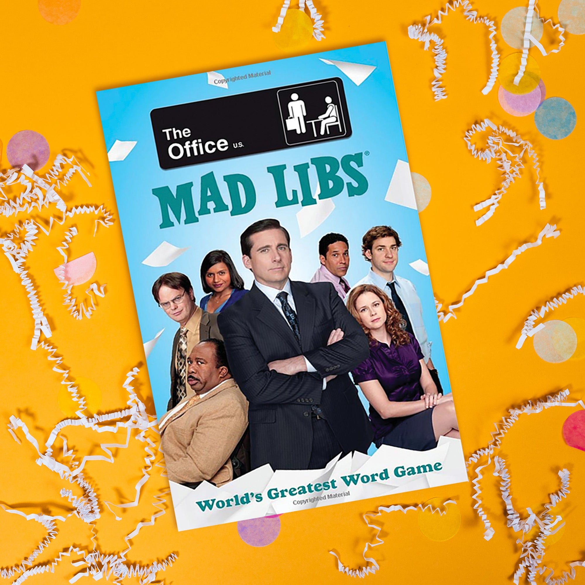 On a summery mustard background sits a book with white crinkle and big, colorful confeetti scattered around. This The Office inspired game book has a picture of various characters from The Office and says "The Office," "MAD LIBS" and "World's Greatest Word Game" in a teal font.