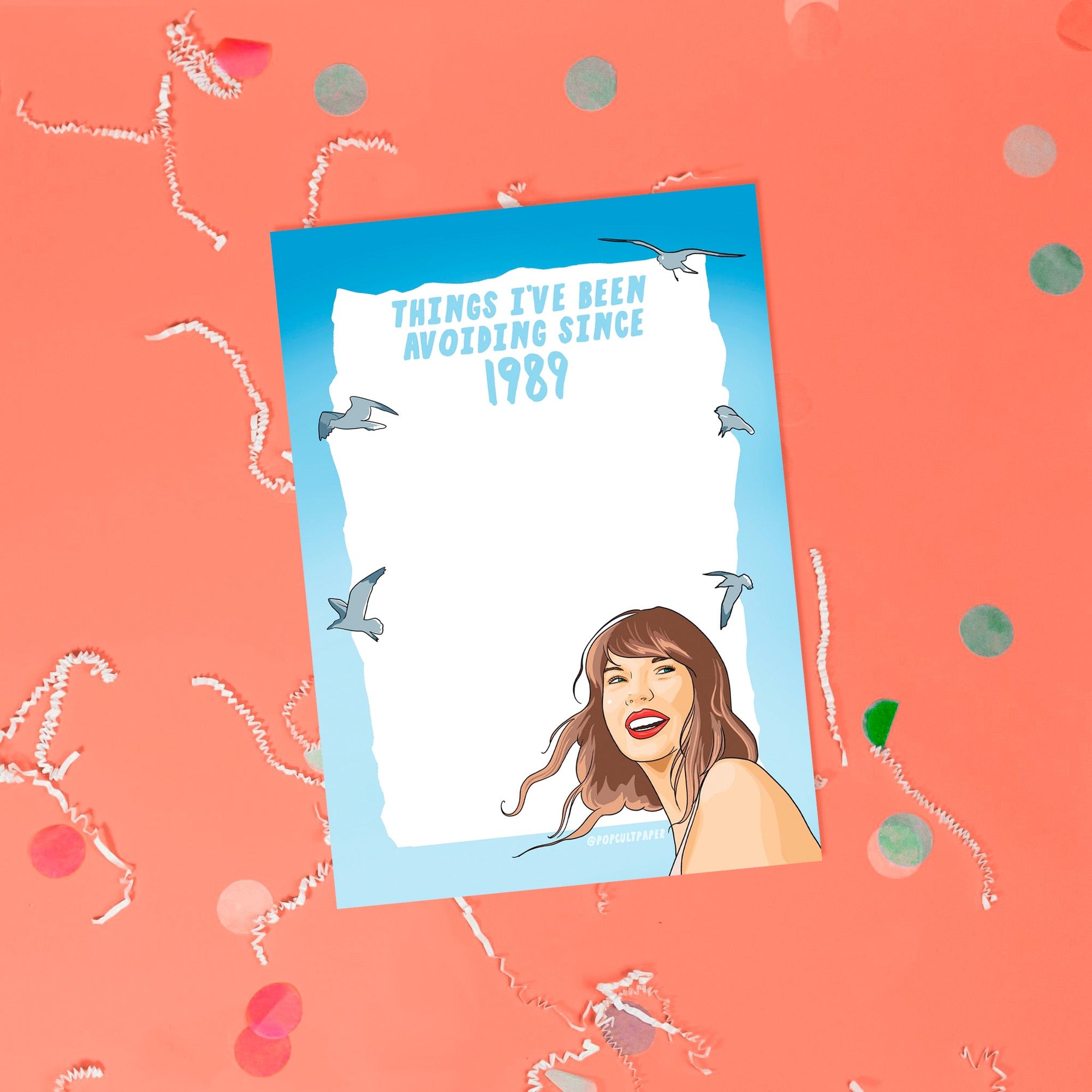 On a coral pink background sits a notepad with white crinkle and big, colorful confetti scattered around. This Taylor Swift inspired notepad is in shades of blues with a white background and it says at the top "THINGS I'VE BEEN AVOIDING SINCE 1989" in blue lettering and there is an illustration of Taylor Swift at the bottom with seagulls flying around.