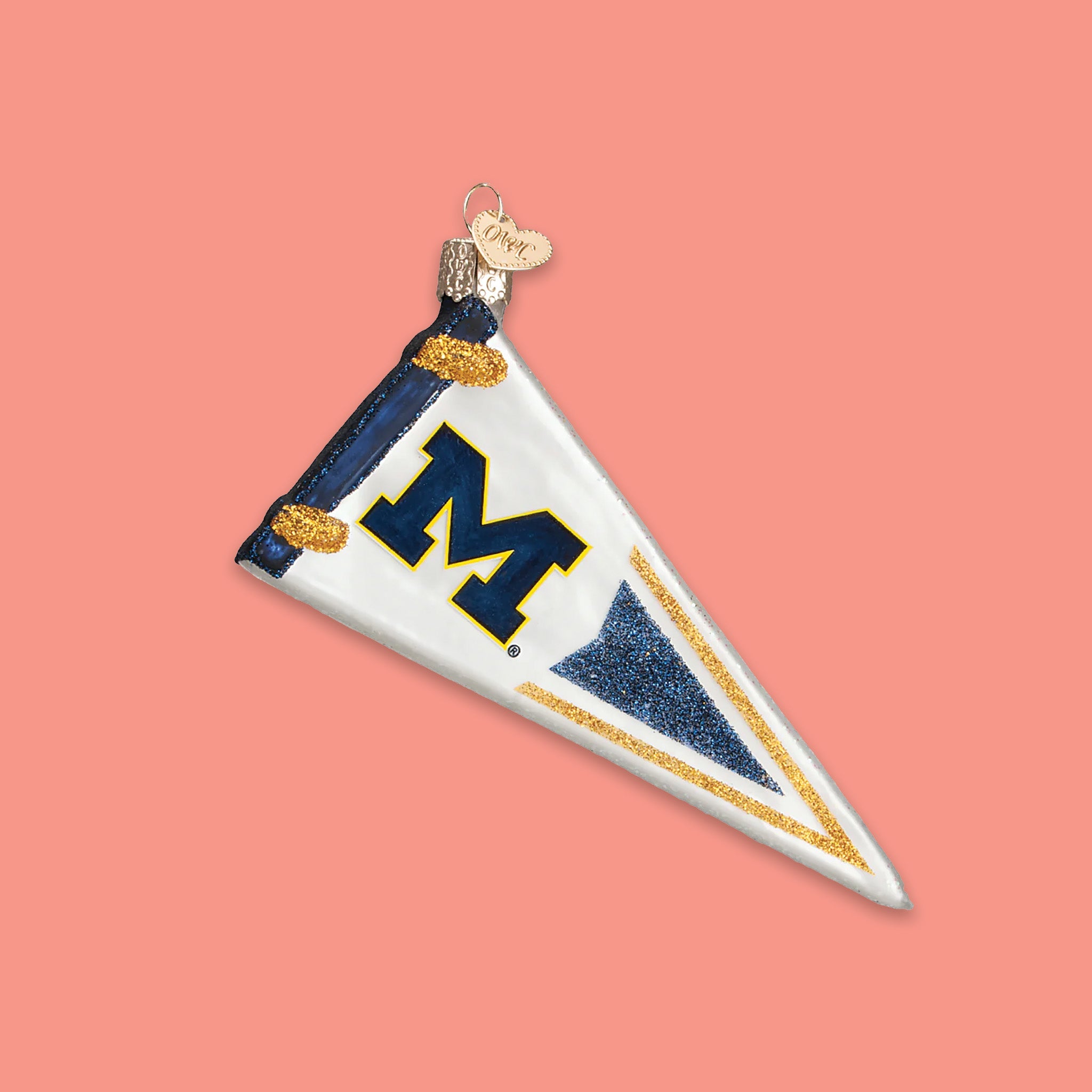 On a coral pink background sits a maize and navy University of Michigan helmet glass ornament.