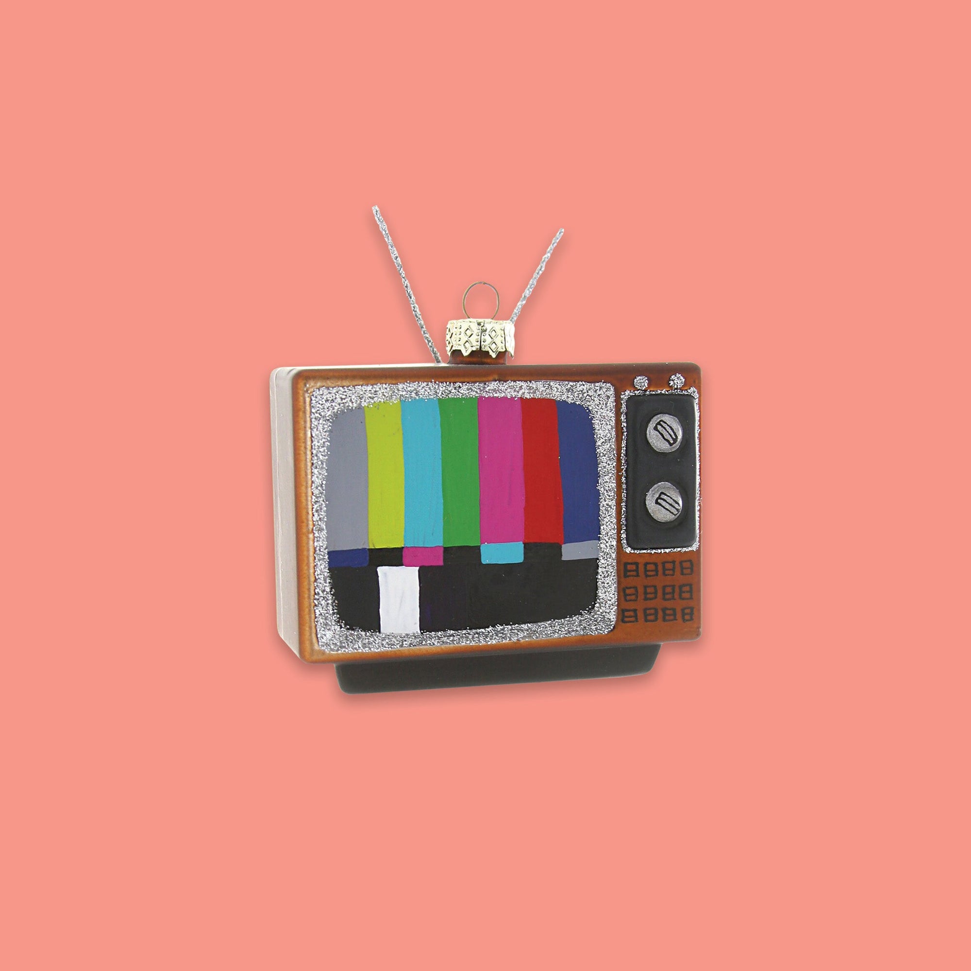 On a coral pink background sits an ornament. This glass ornament is of a vintage tv with rabbit ears.