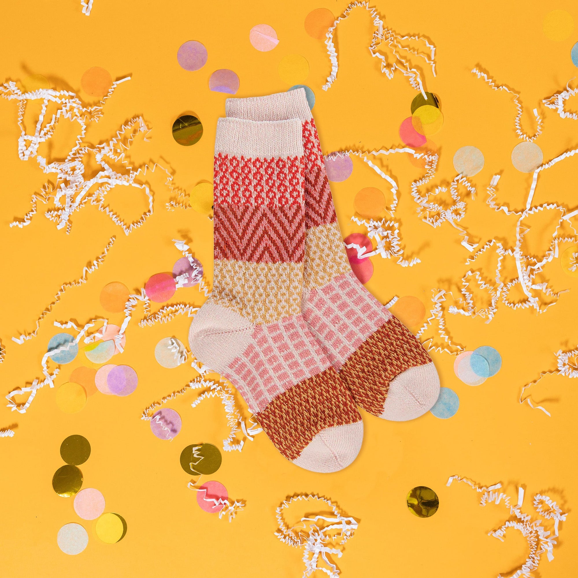 On an sunny mustard background sits the world's softest socks with different patterns in modern fall colors, including orangey-red, rust, peach, and mustard. There are white crinkle and big, colorful confetti scattered around.