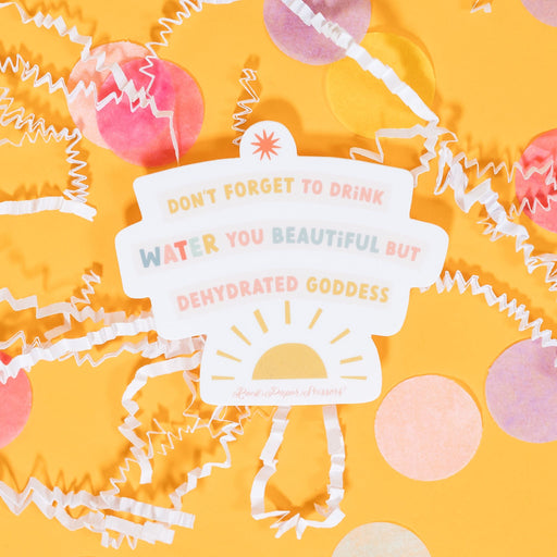 On a sunny mustard background sits a sticker with white crinkle and big, colorful confetti scattered around. This white sticker has a handdrawn illustration of a red star at the top and a half yellow sun at the bottom. It says "Don't Forget To Drink Water You Beautiful But Dehydrated Goddess" in different colors of yellow, pink, blue, red and mustard yellow in handdrawn block lettering. At the bottom it says "Rock Paper Scissors" in handdrawn script lettering. 2"-3"