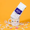 On a sunny mustard background sits a mug and a bag of coffee with white crinkle and big, colorful confetti scattered around.  The mug is a large white mug with colorful collegiate font that says "Ann Arbor" with "ROCK PAPER SCISSORS" below it. The white bag of coffee sits atop the mug. The coffee is Rock Paper Scissors 'Hail Yes!' in white hand lettering on a brilliant blue label. It is 'BLUEBERRY CRUMBLE GROUND COFFEE'. Small batch roasted, fruit forward, balanced w/ aromatic vanilla. Net Wt. 12 oz. (340g)